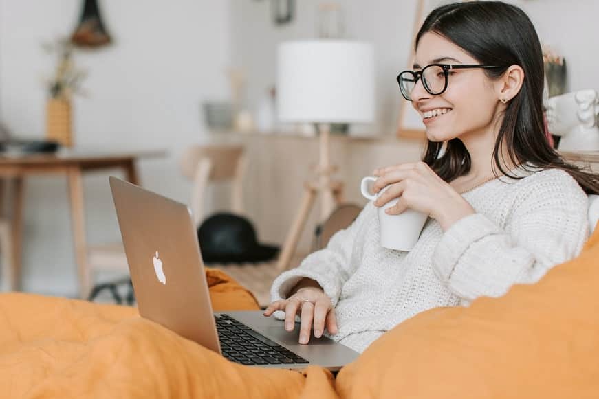 אישה צעירה עם שיער שחור שותה קפה ומסתכלת במחשב שלה על דברים שונים