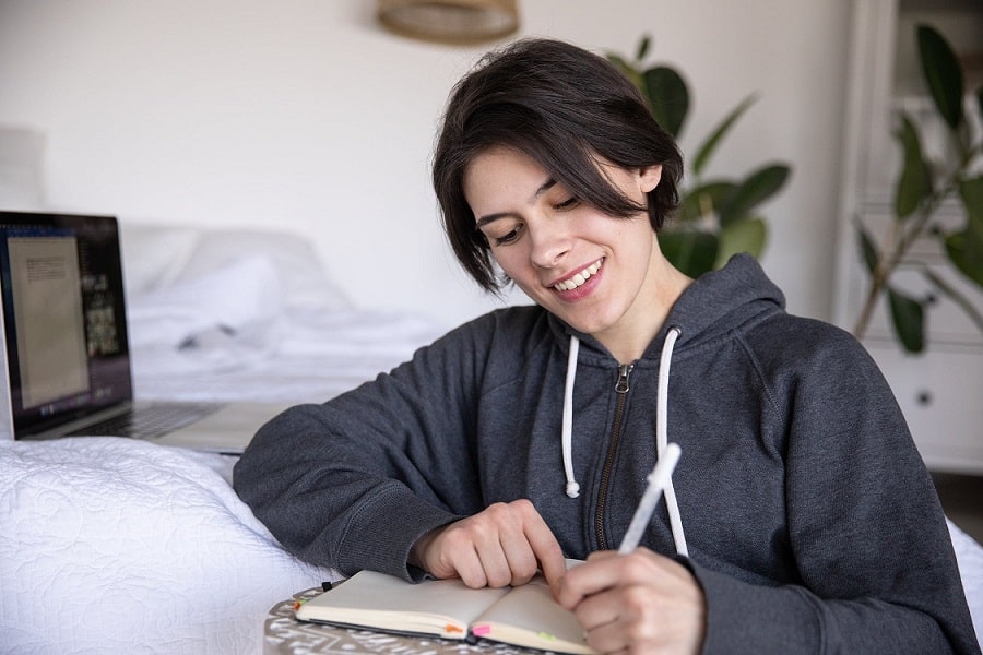 בחורה עם שיער שחור וקצר כותבת הערות בתוך מחברת עם עט בצבע לבן