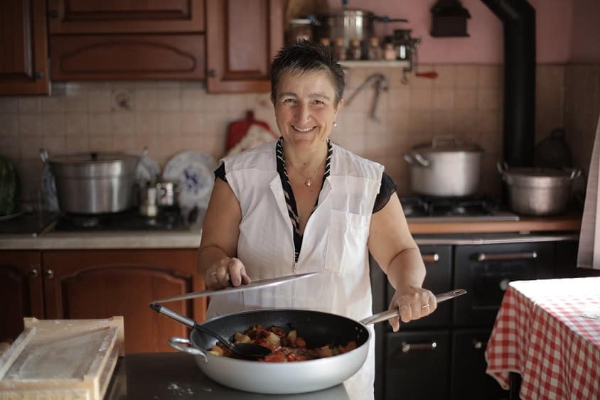 בשלנית מבוגרת מראה את הבישולים שלה במטבח הביתי ומחייכת