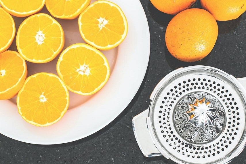 תפוזים טריים פרוסים לחצי שוכבים ליד מכשיר לסחיטה ידנית של מיץ