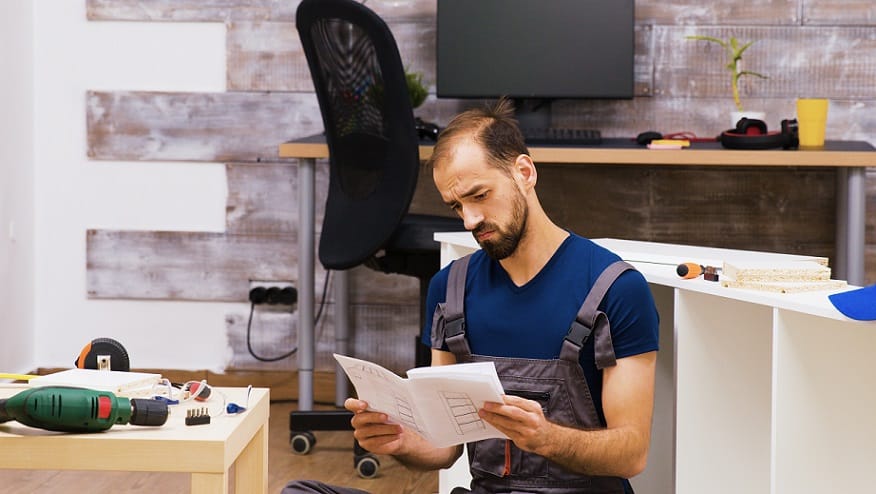 גבר צעיר ומקריח קורא הוראות התקנה של משהו וחושב