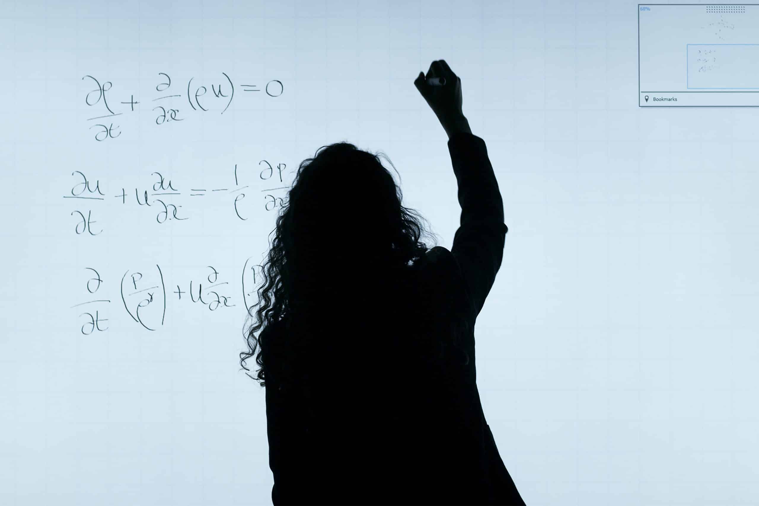 תצלום מאחורה של בחורה שכותבת נוסחאות מתמטיות על לוח מואר