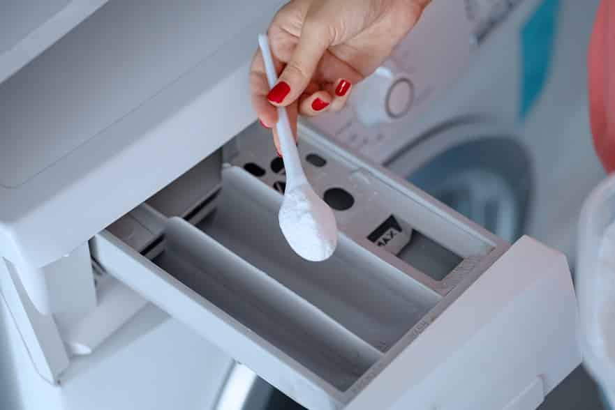 יד של בחורה מכניסה חומר ניקוי למכונת הכביסה שלה