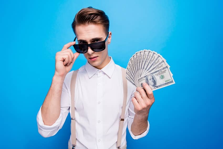 בחור צעיר מחזיק שטרות של כסף ביד על רקע כחול