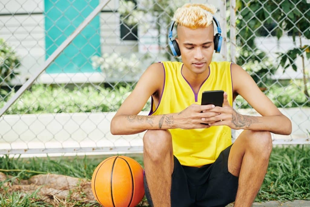שחקן כדורסל צעיר יושב בטלפון בהפסקה עם אוזניות ספורט