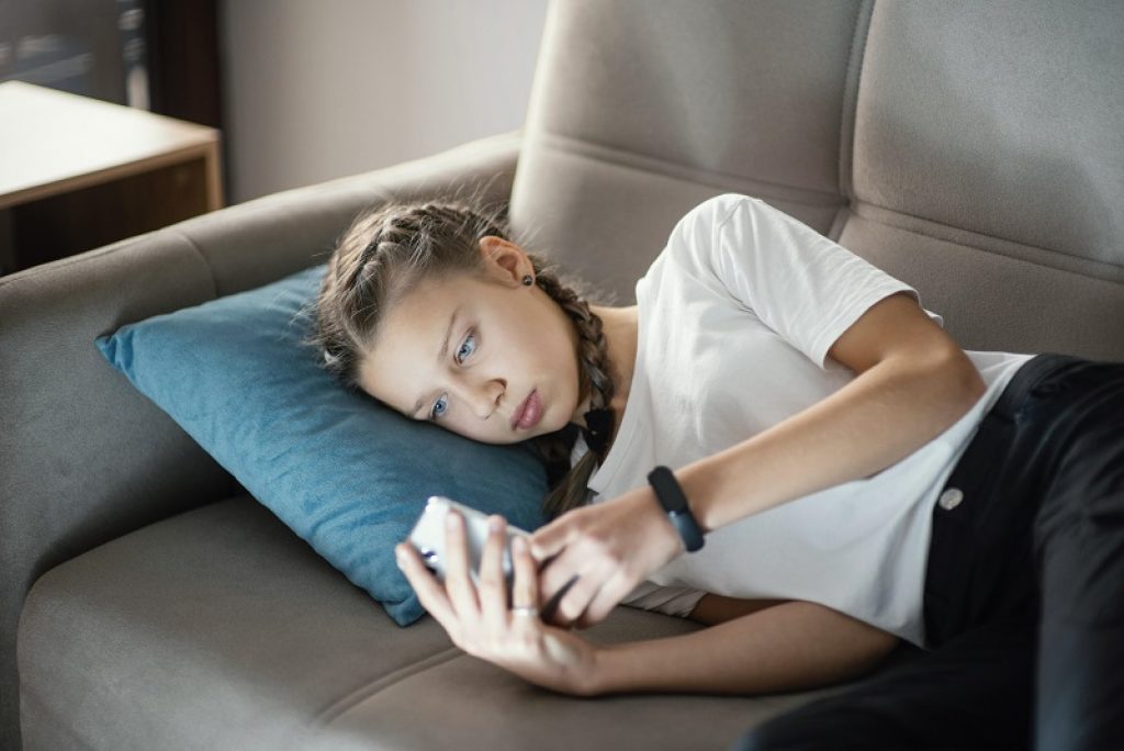 נערה שוכבת על הספה עם כרית כחולה וטלפון ביד