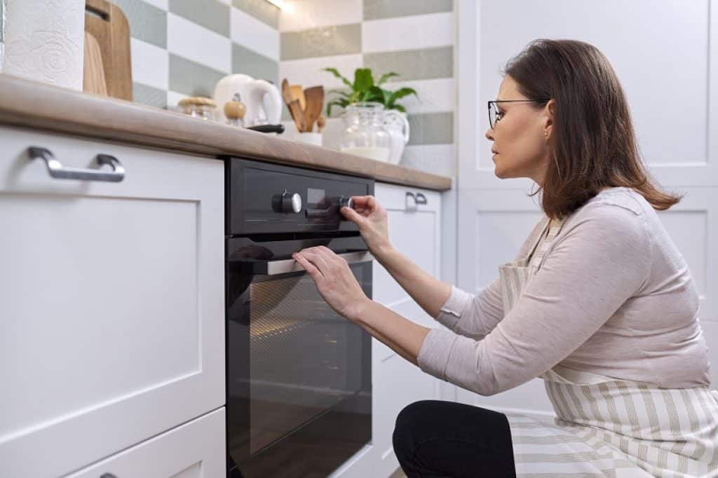 אישה מתכופפת כדי לשנות תוכנית בתנור בנוי