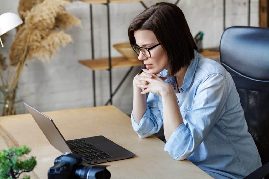 אישה עם משקפיים וחולצה כחולה יושבת מול מחשב נייד