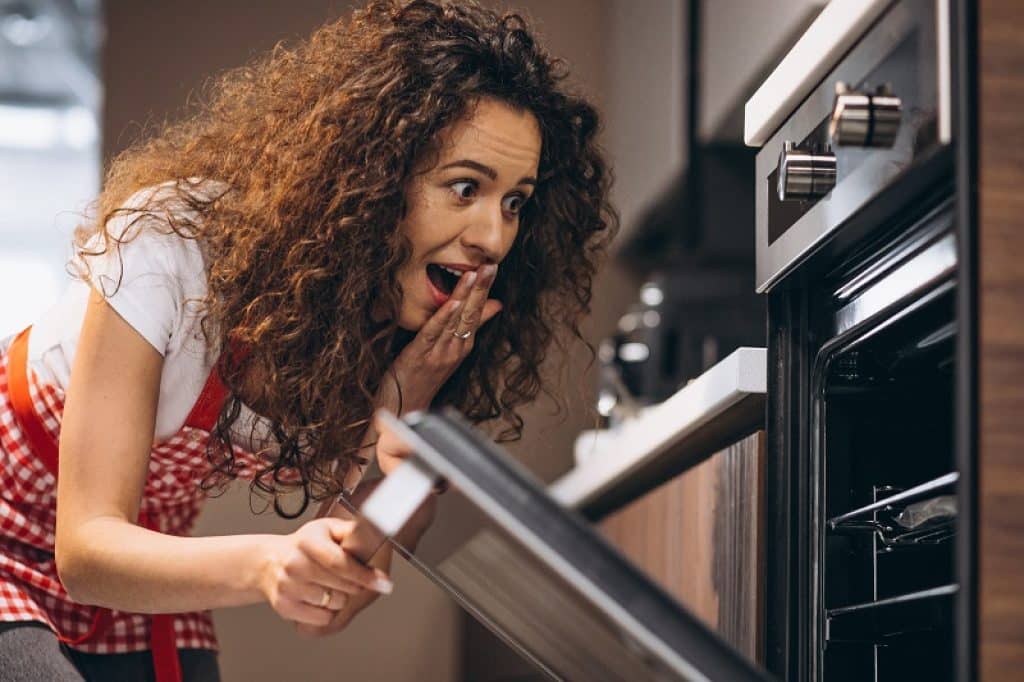 אישה עם תלתלים וסינר אדום שמה יד על הפה