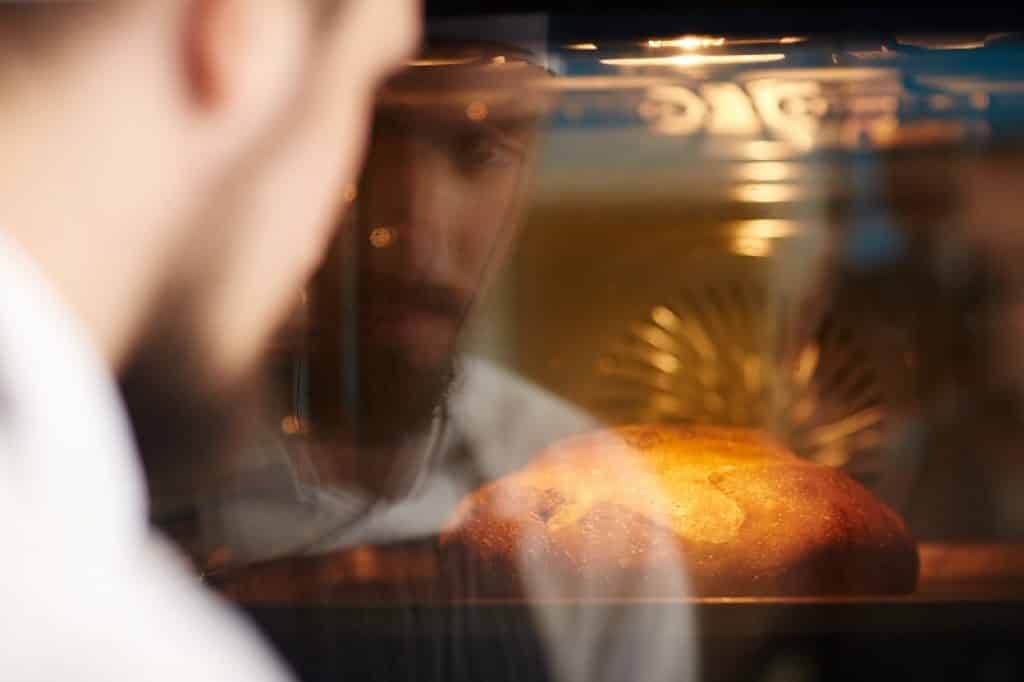 איש עם סינר מסתכל על הלחם שהכין בזמן האפייה