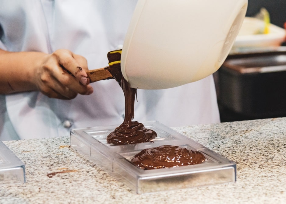איש שופך שוקולד מומס מתוך קערה לתבנית פלסטיק במטבח