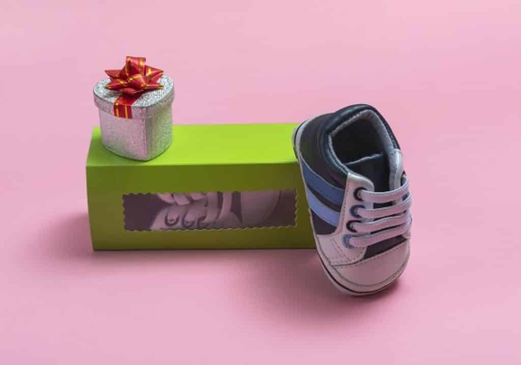 נעל של תינוק נשענת על קופסא ירוקה עם קופסת מתנה קטנה רקע ורוד