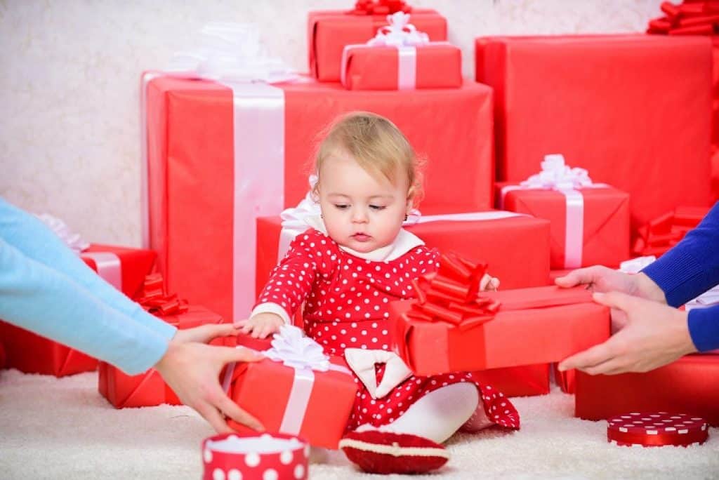 תינוקת בשמלה אדומה יושבת וסביבה ערמת מתנות בעטיפה אדומה וסרטים לבנים