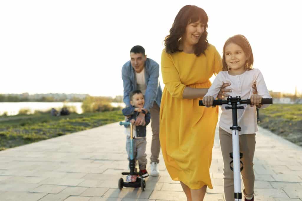 משפחה עם אבא אמא ושני ילדים רוכבים על קורקינט ברחוב