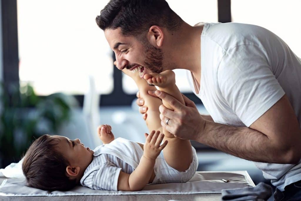 אבא משחק עם התינוק שלו ומחייך בזמן שהוא מחליף לו חיתול