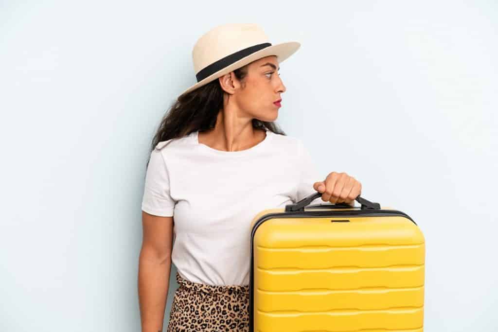 בחורה בחולצה לבנה וכובע מחזיקה מזוודה צהובה מסתכלת הצידה רקע לבן