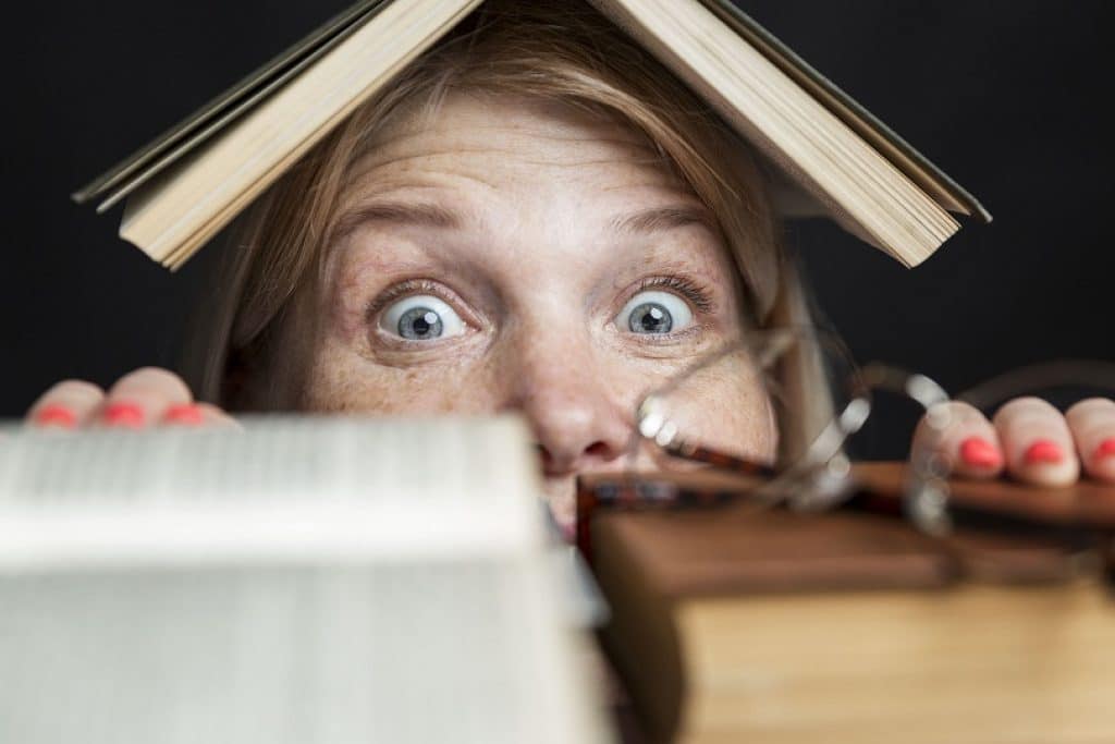 בחורה עם ספר על הראש מציצה מעל ערמת ספרים ישנים מבט מפוחד