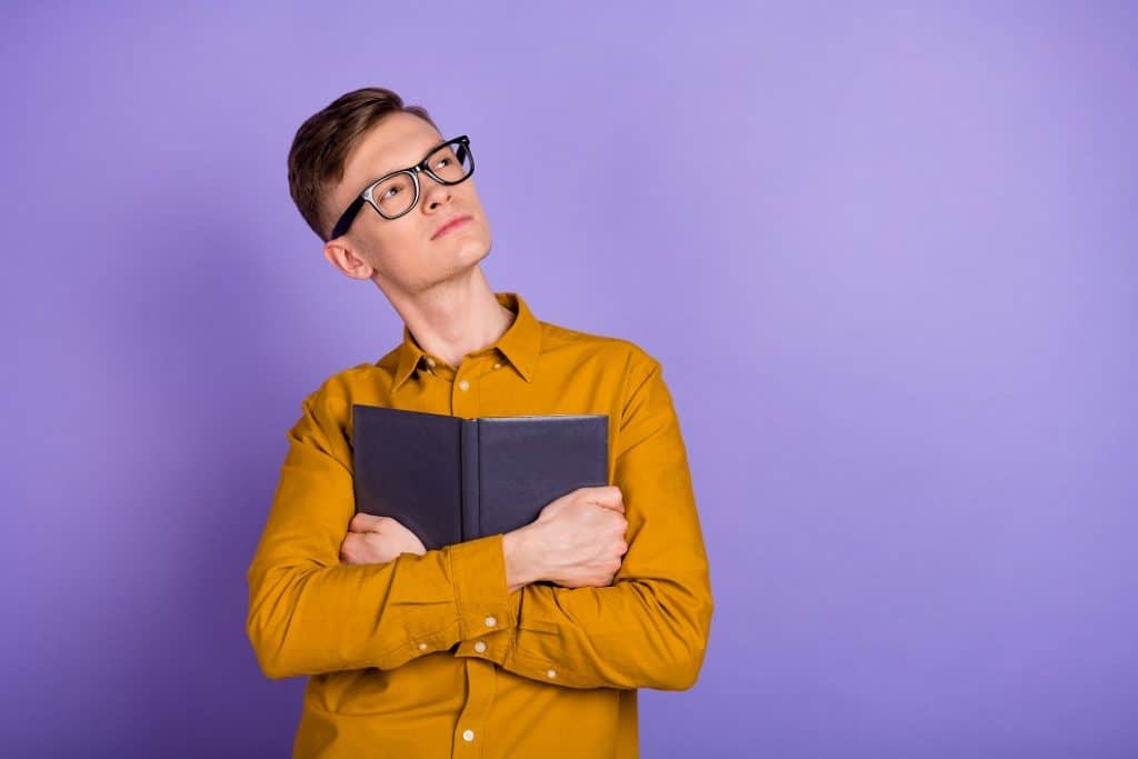 בחור עם משקפיים וחולצה צהובה מחזיק ספר שחור וחושב רקע סגול