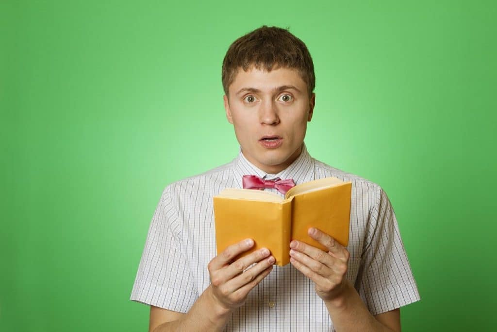 בחור קורא ספר אימה עם עטיפה צהובה מבט מבוהל רקע ירוק
