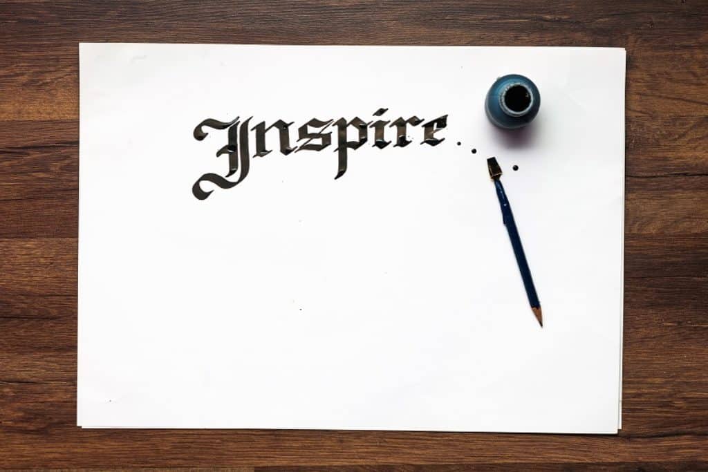 דף לבן עם המילה השראה כתובה באנגלית בדיו שחורה עם עט וקסת