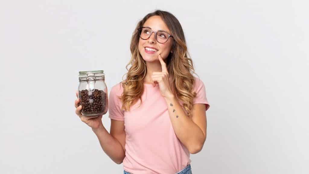 אישה עם חולצה וורודה ומשקפיים מחזיקה צנצנת עם פולי קפה