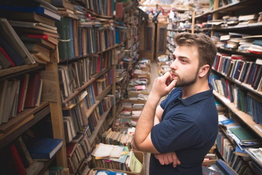 בחור בחולצה כחולה עומד ומסתכל על ספרים ברקע מדפים עמוסים ספרים