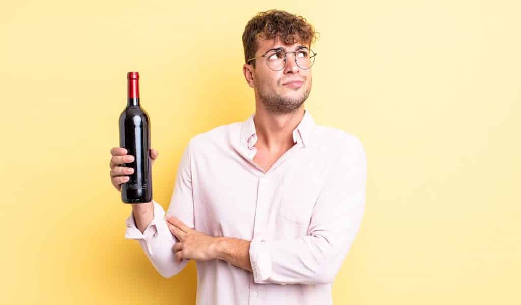 בחור בחולצה מכופתרת ומשקפיים מחזיק בקבוק יין וחושב רקע צהוב