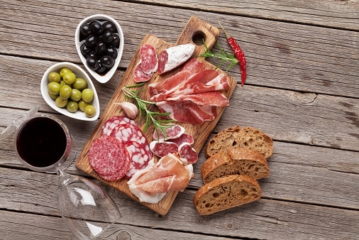 מגש בשרים עם זיתים לחם וכוס יין אדום על רקע שולחן עץ