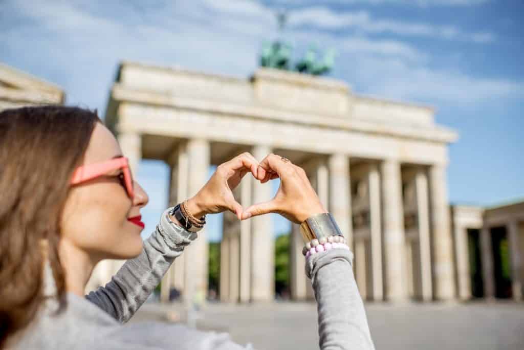 בחורה מחזיקה את הידיים בצורת לב וברקע אתר תיירות בברלין