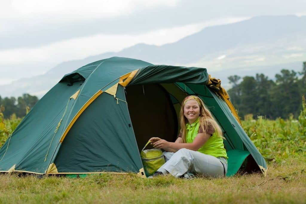 בחורה מחייכת יושבת בפתח אוהל פתיחה מהירה ברקע עצים וטבע