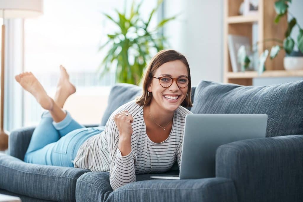 בחורה עם משקפיים שוכבת על ספה ומסתכלת במחשב נייד מחייכת