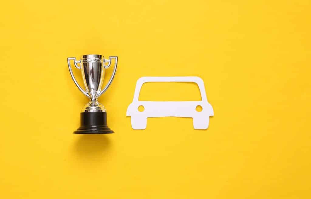 גזיר נייר בצורת מכונית ולידו גביע זהב על רקע צהוב