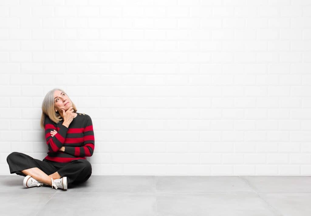 אישה בסוודר אדום יושבת על הרצפה חושבת ומסתכלת על קיר לבן