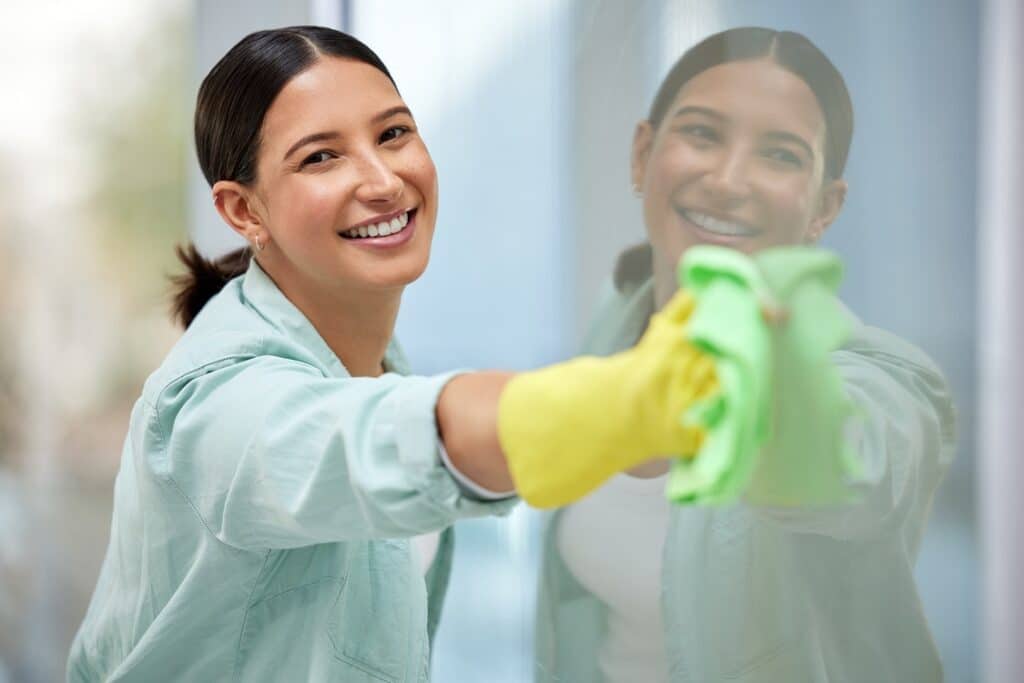 אישה עם כפפות צהובות ומטלית מנקה חלון ומחייכת