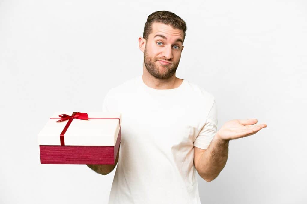 בחור מחזיק קופסת מתנה מושך בכתפיים וחושב רקע לבן