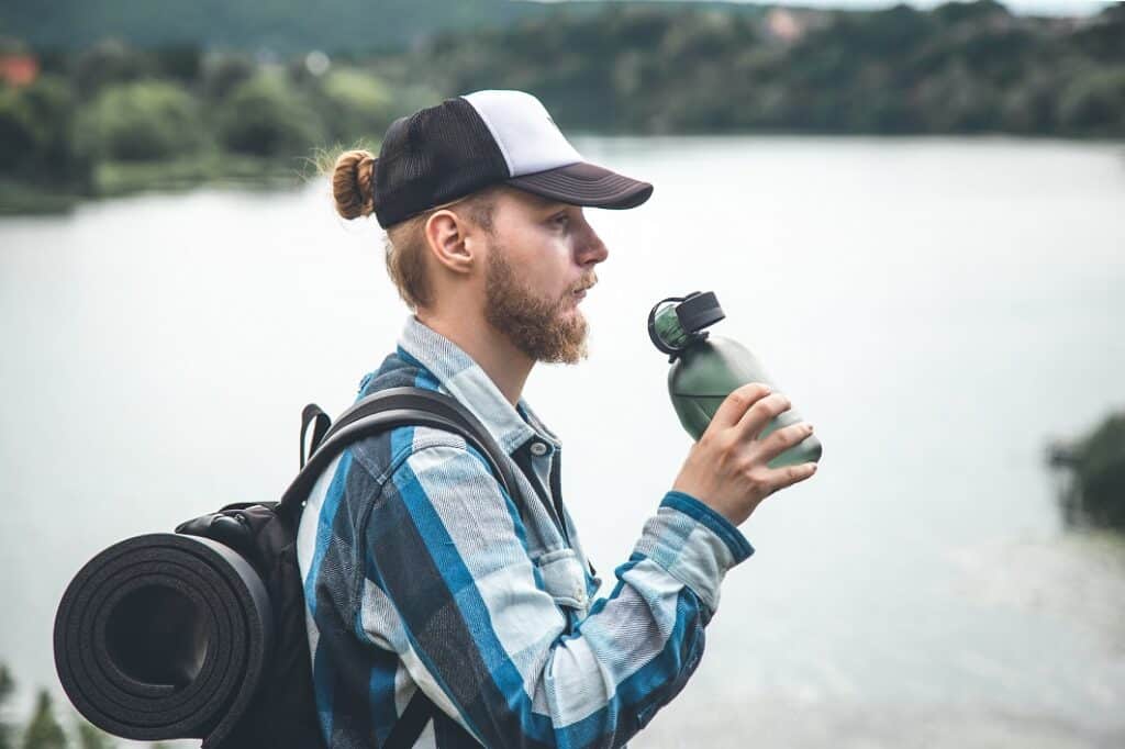 בחור מטייל בטבע עם כובע ותיק מחזיק בקבוק מים 