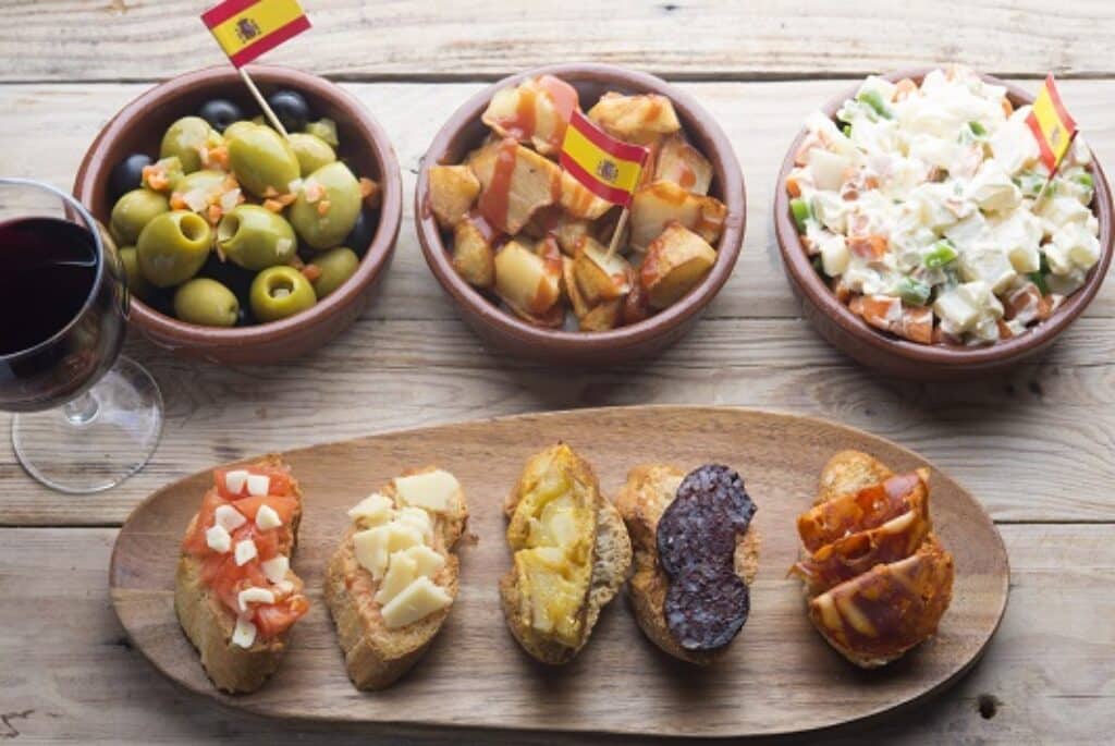 מגוון מאכלי טאפאס עם דגלי ספרד בקעריות מונחים על שולחן עץ