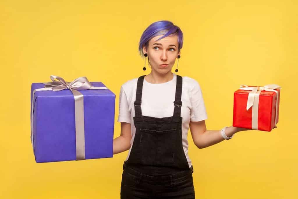 בחורה עם דיער סגול ואוברול שחור מחזיקה שתי קופסאות מתנה רקע צהוב
