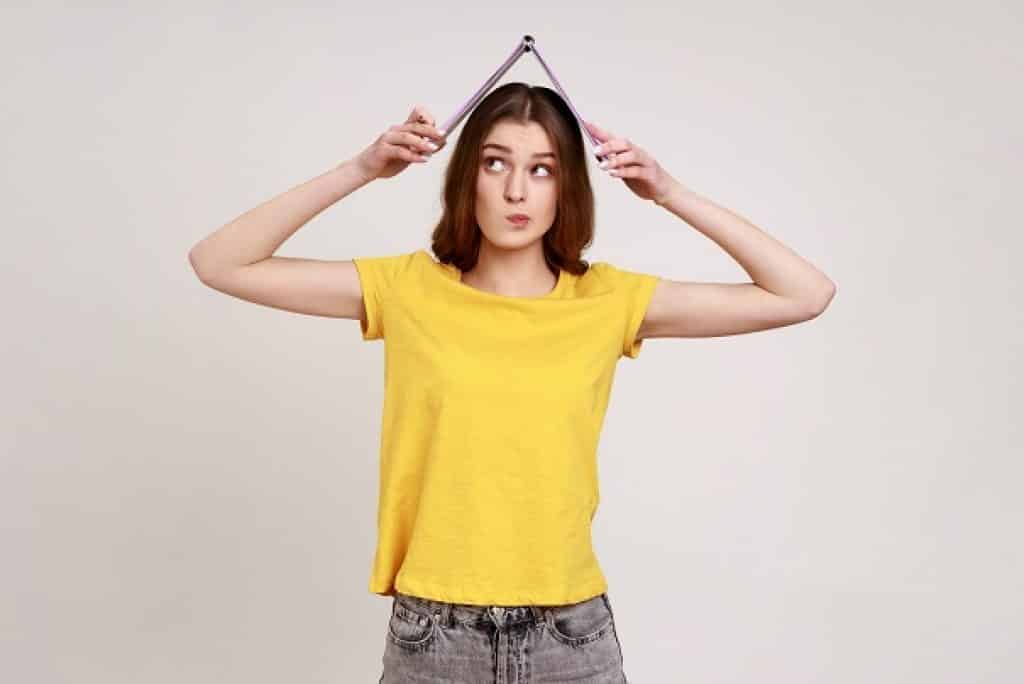 בחורה עם חולצה צהובה מחזיקה ספר פתוח על הראש רקע לבן