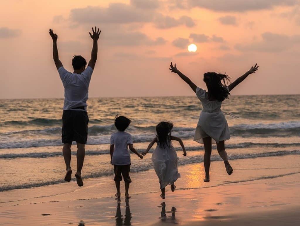 משפחה הורים ושני ילדים בחוף הים בשקיעה קופצים בשמחה באוויר
