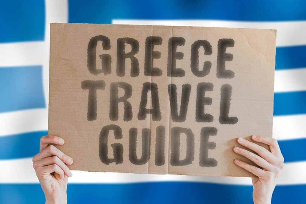 שלט קרטון שעליו כתוב מדריך טיולים ביוון וברקע פסים בכחול ולבן