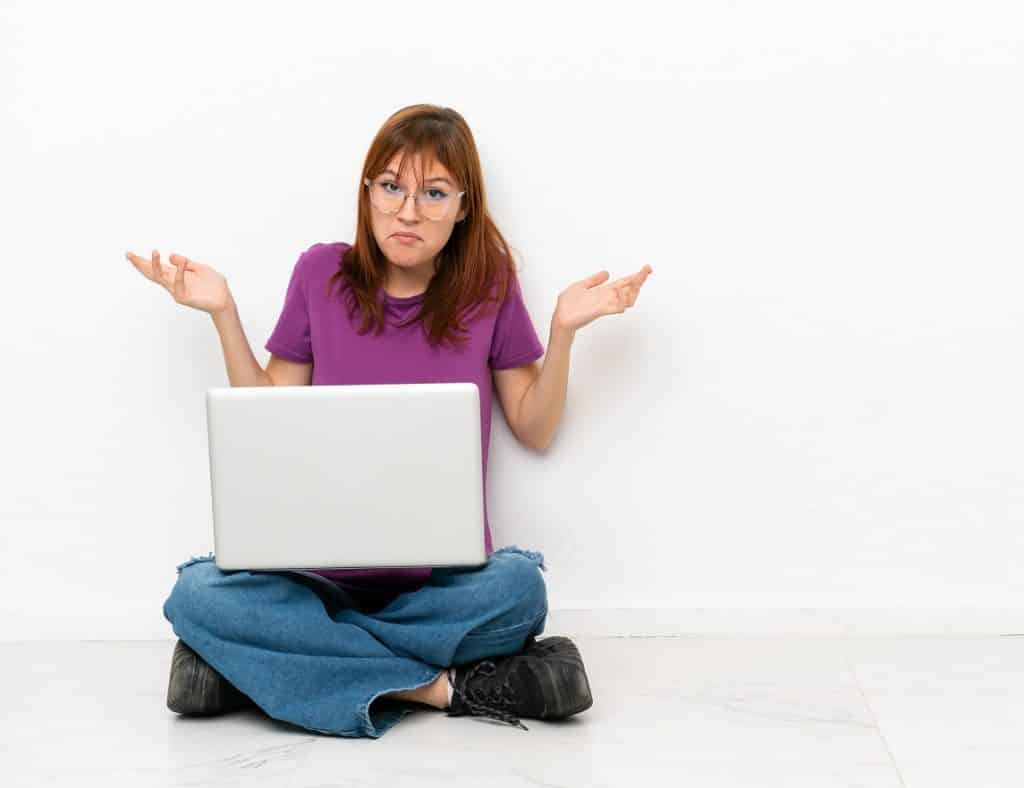 בחורה בחולצה סגולה ומשקפיים יושבת על הרצפה עם מחשב נייד מלבטת 
