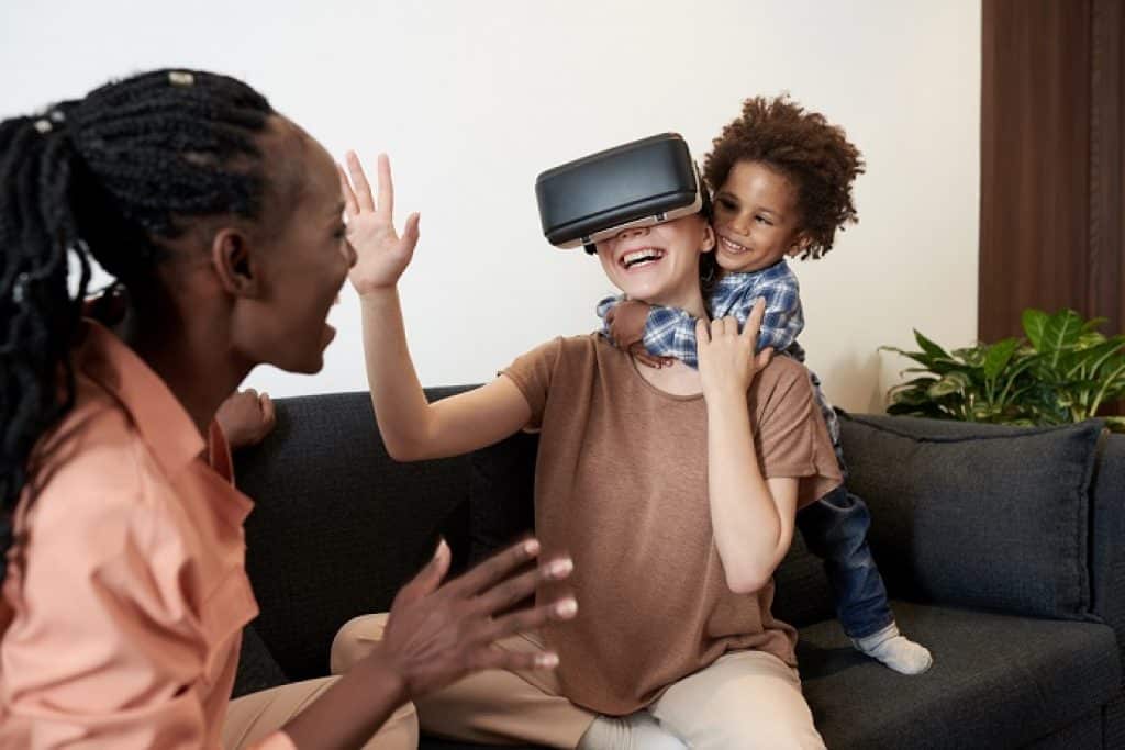 בחורה עם משקפי VR יושבת על ספה צוחקת ילד מחייך עם אישה נוספת