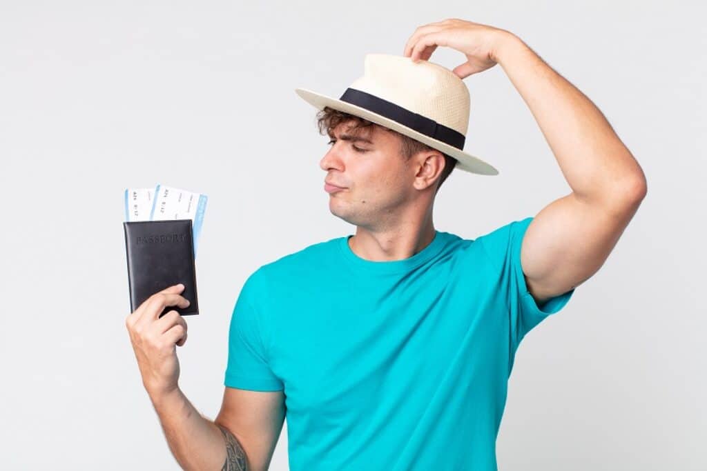 בחור בחולצה תכלת וכובע קש מחזיק דרכון וכרטיסי טיסה וחושב