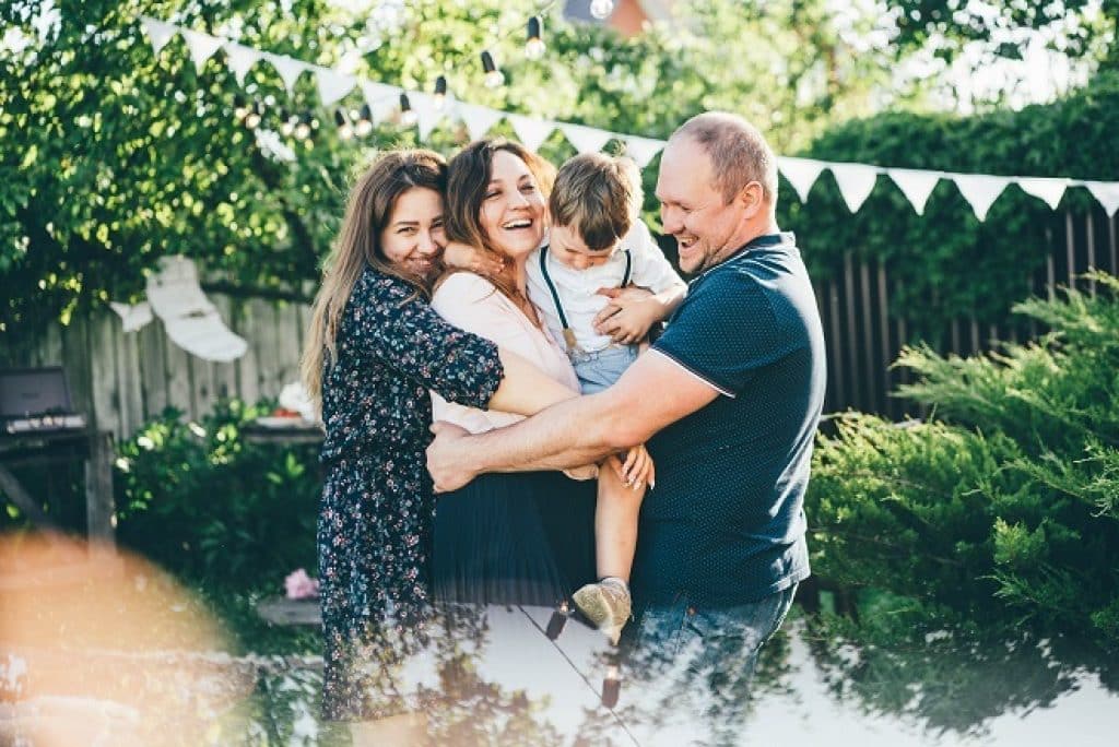  משפחה של ארבעה אנשים מאושרת מחייכת ומתחבקת ברקע גינה