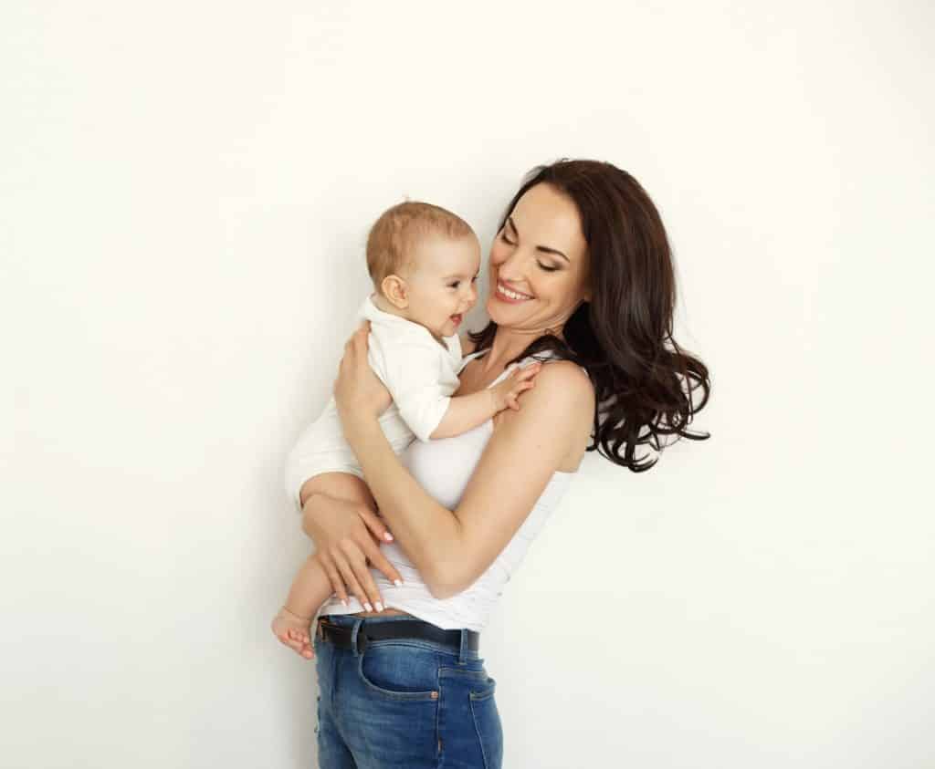 אמא עם ג'ינס וגופיה לבנה מחייכת ומחזיקה  תינוק צוחק  