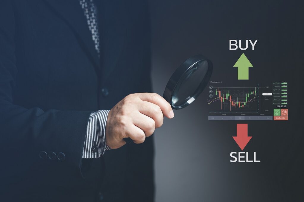 יד מחזיקה זכוכית מגדלת מעל מסך של מניות בבורסה עם המילים קנייה ומכירה
