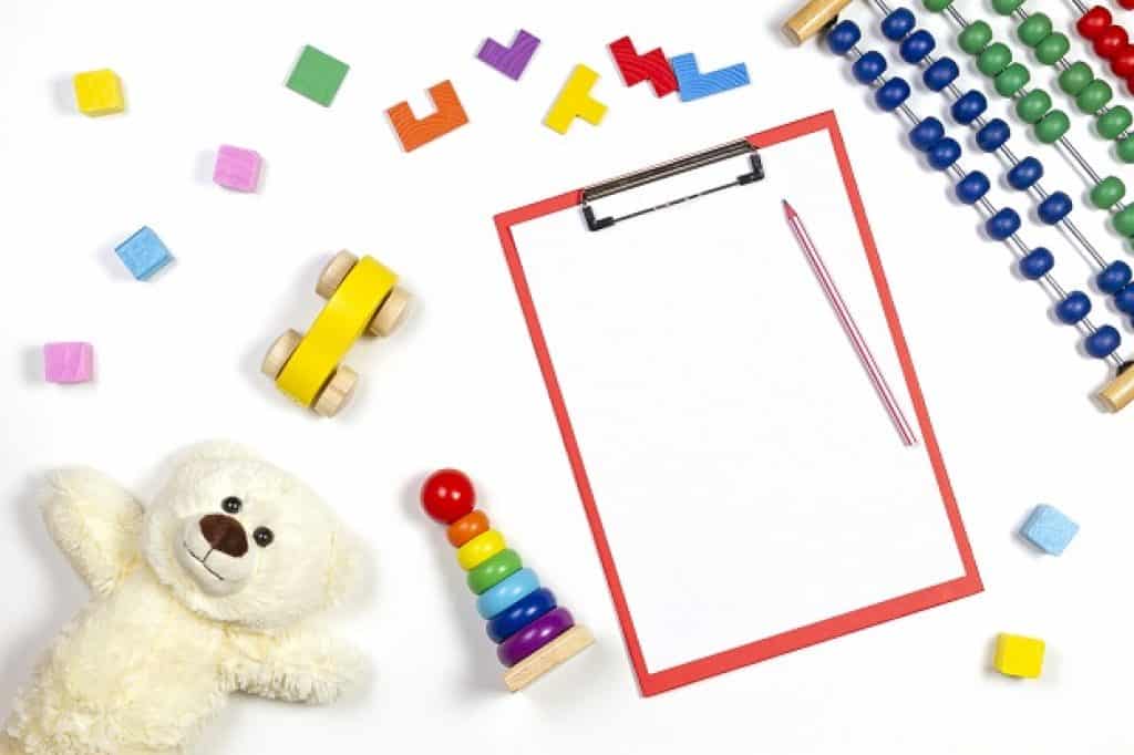 לוח כתיבה עם עט אדום וסביבו משחקים דובון וקוביות לילדים רקע לבן