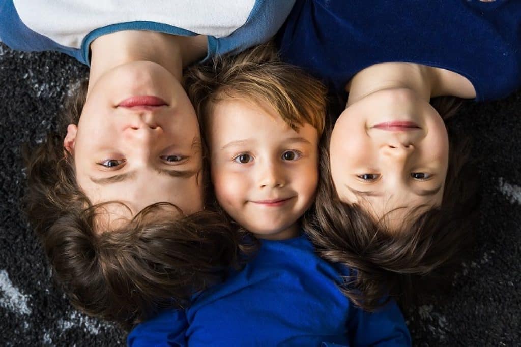 שלושה ילדים בגילאים שונים שוכפים ראש אל ראש ומחייכים