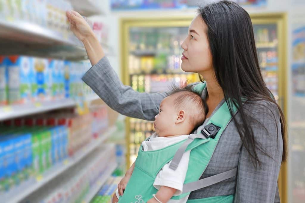 אישה צעירה עם תינוק במנשא תכלת בחנות בוחרת מוצרי תינוקות